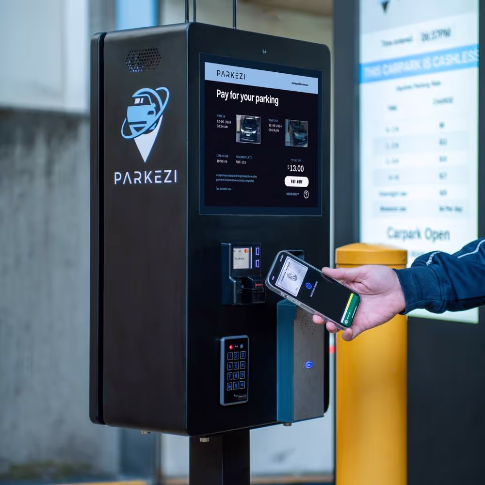 A person uses a smartphone to make a contactless payment at a parking payment machine.
