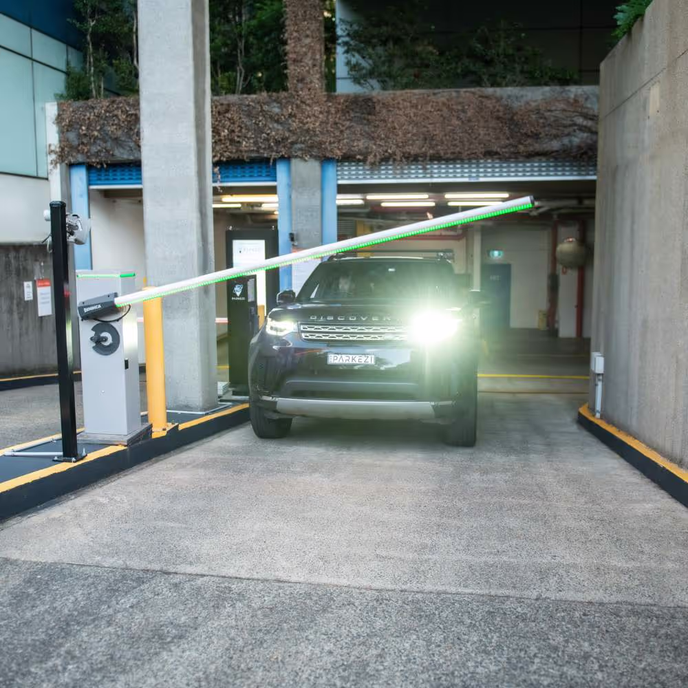 A car with bright headlights drives through a parking lot barrier gate.