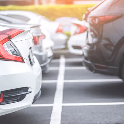 Cars parked in a row in a parking lot, with white and black vehicles in view.