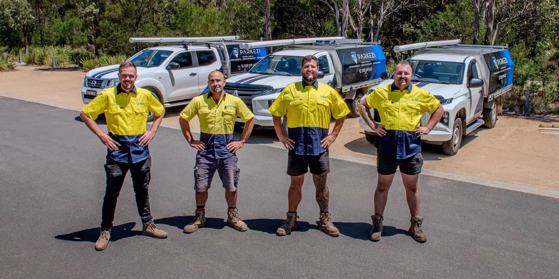 Four workers in uniform stand smiling in front of parked utility vehicles on a sunny day.