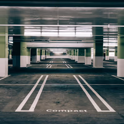 Empty underground parking lot with marked spaces and green pillars.